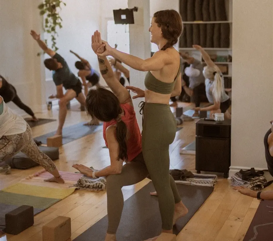 Instructor guiding a student in warrior pose during a Form & Flow class